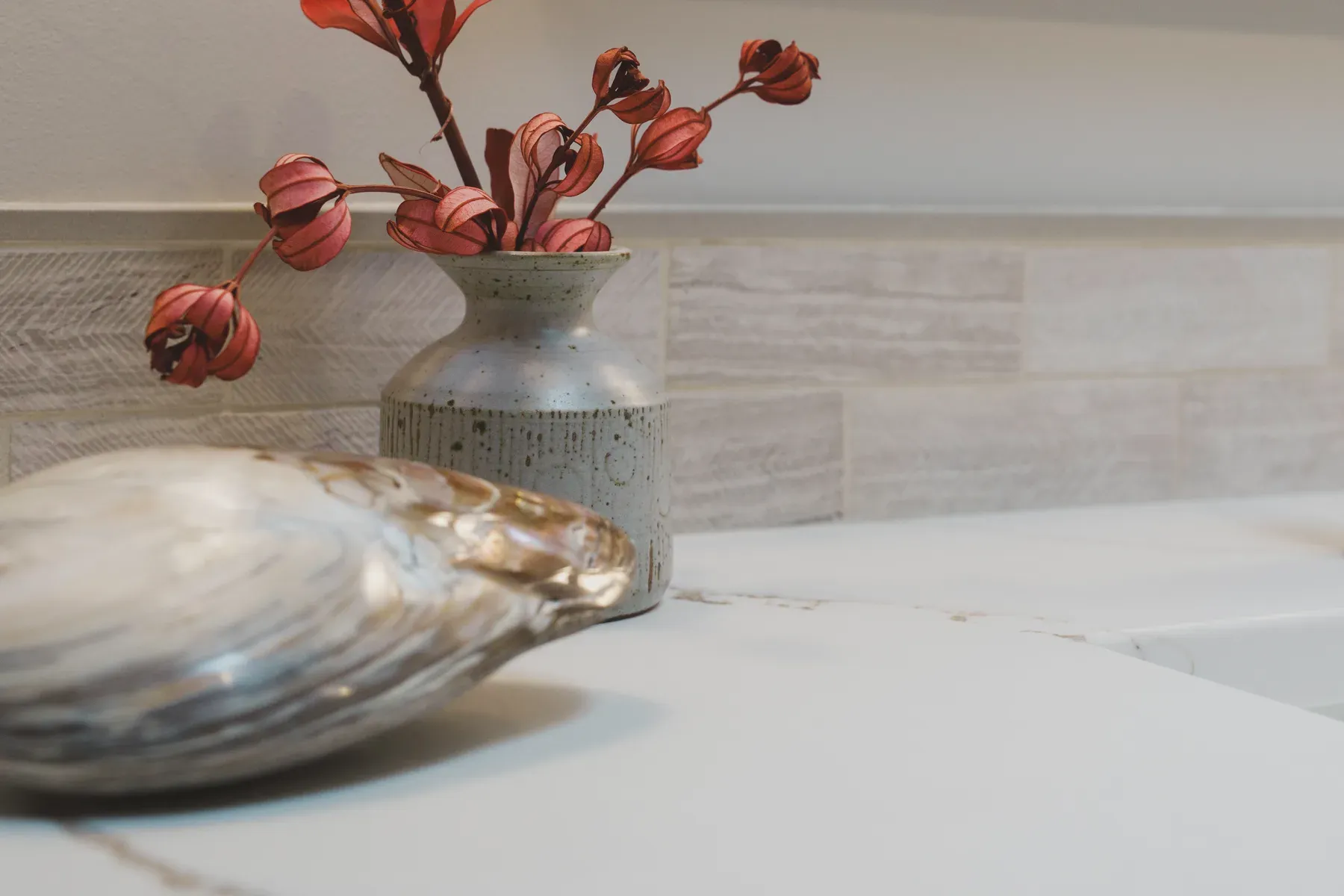 Sculptural red foliage arranged in a ceramic vase on a stone vanity